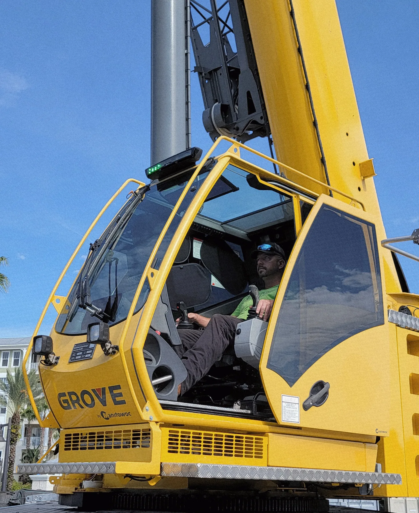 A person seated at the controls inside the open cab of a yellow crane.