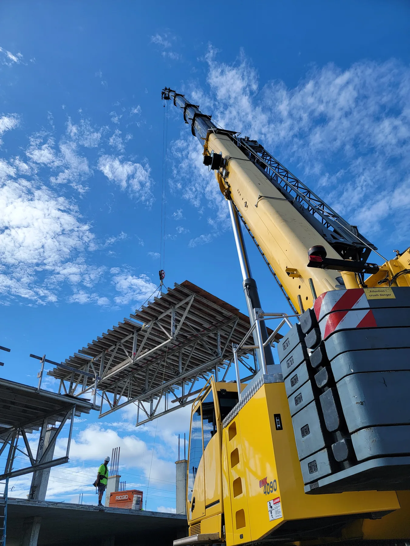 Upward view beside a yellow crane’s boom and stacked counterweights, with a suspended structure above.