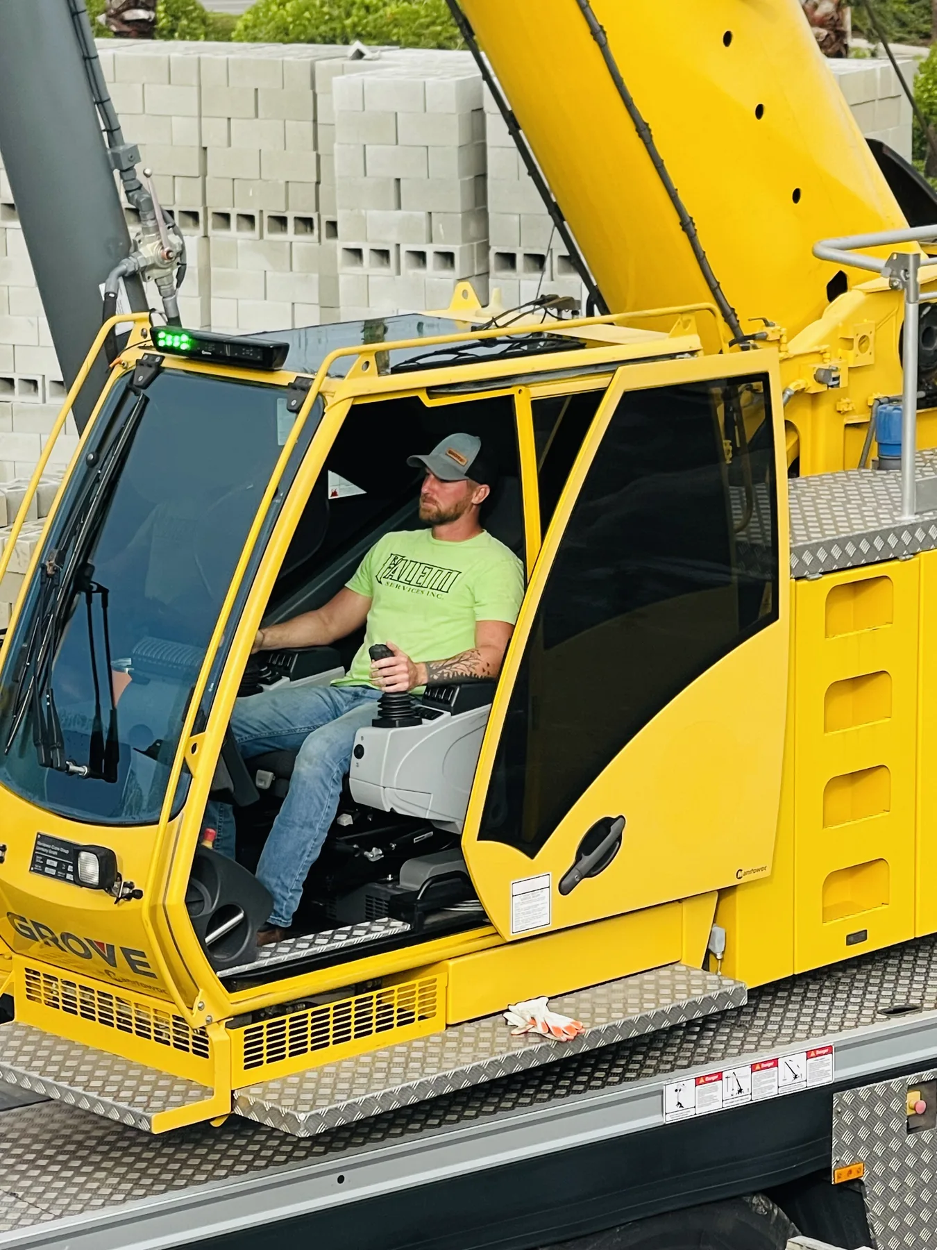 Operator seated in a yellow crane cab, with a hand on a control lever.
