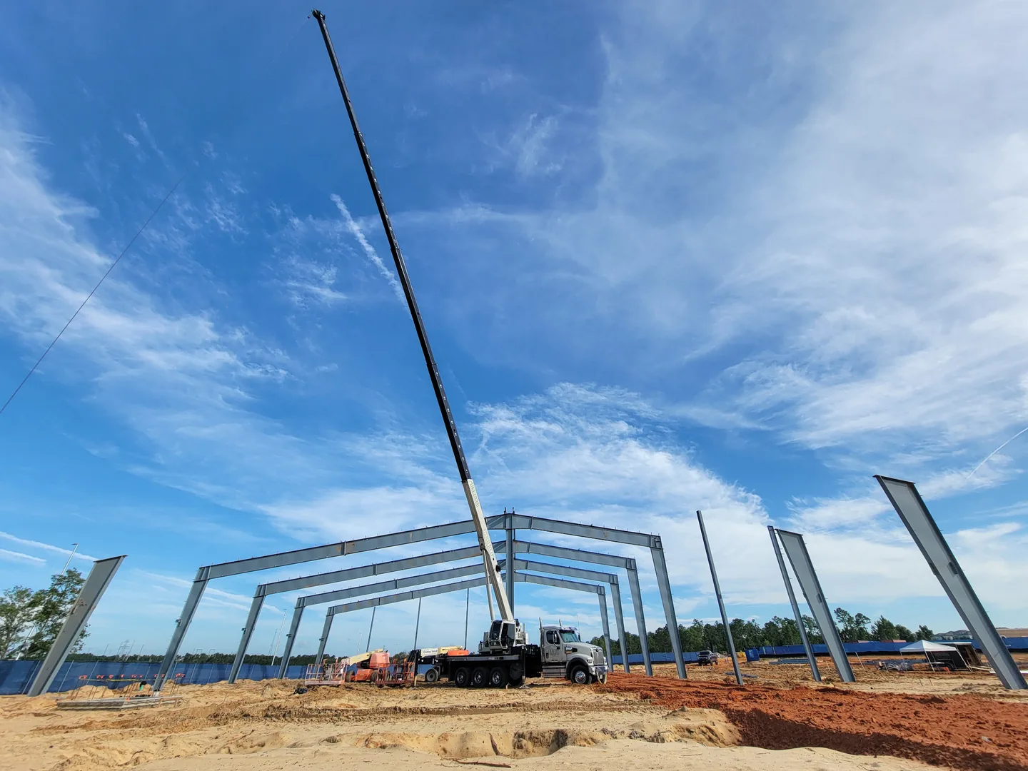White crane truck beneath steel building frames and blue sky.