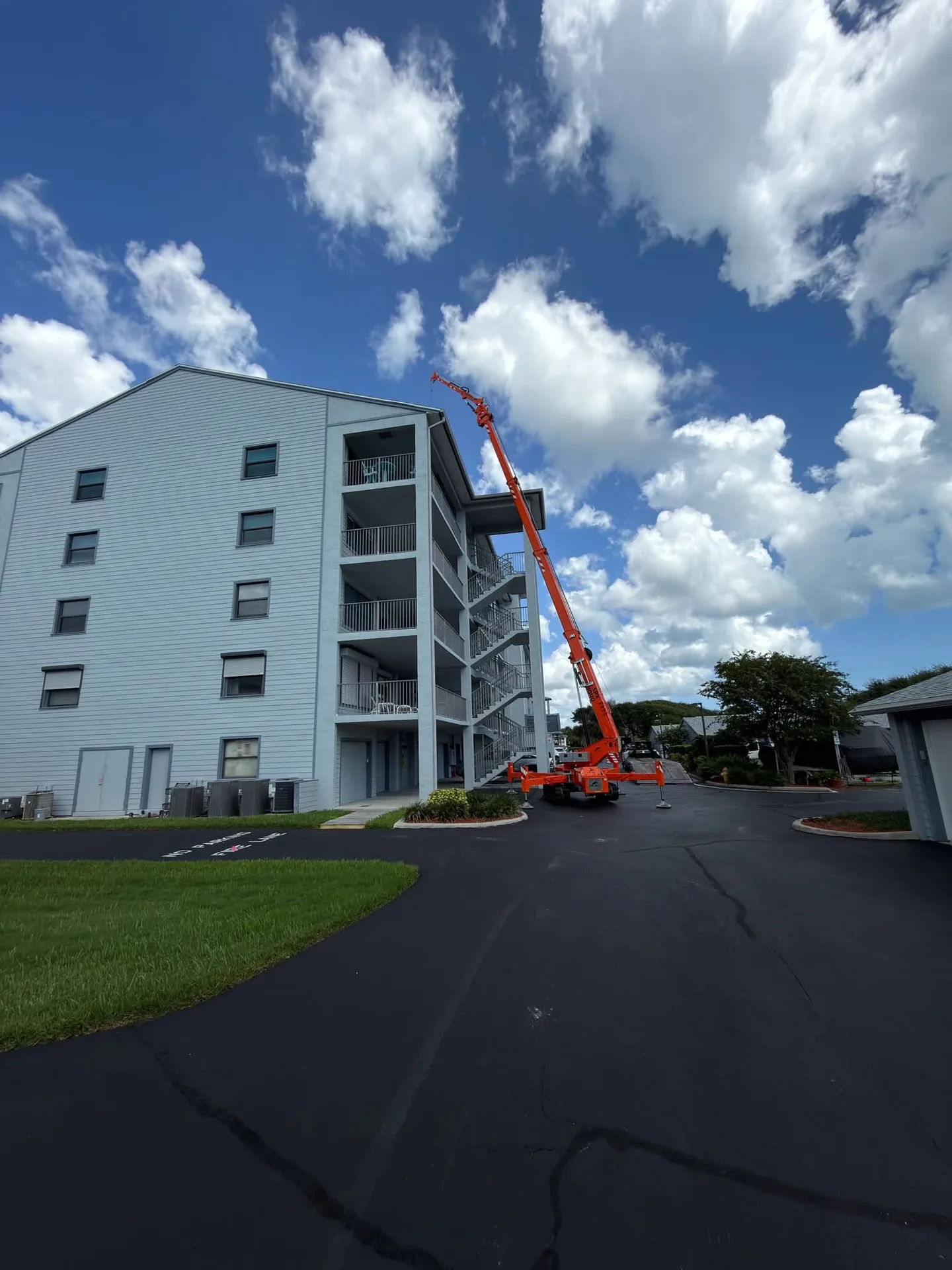 Orange compact crane with its boom raised beside a multi-storey building.