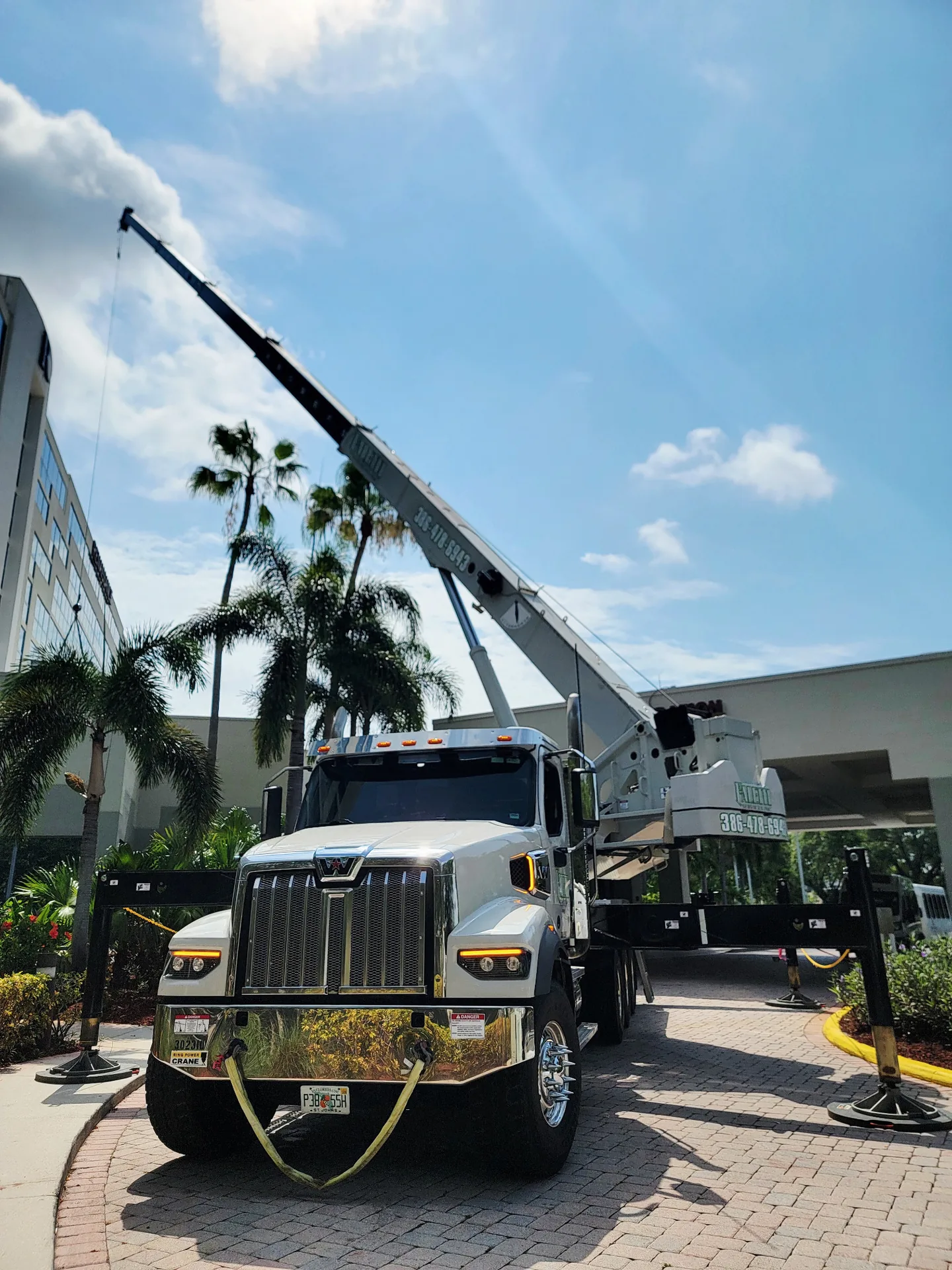 Front view of a white Faletti crane truck with its boom raised beside palm trees.