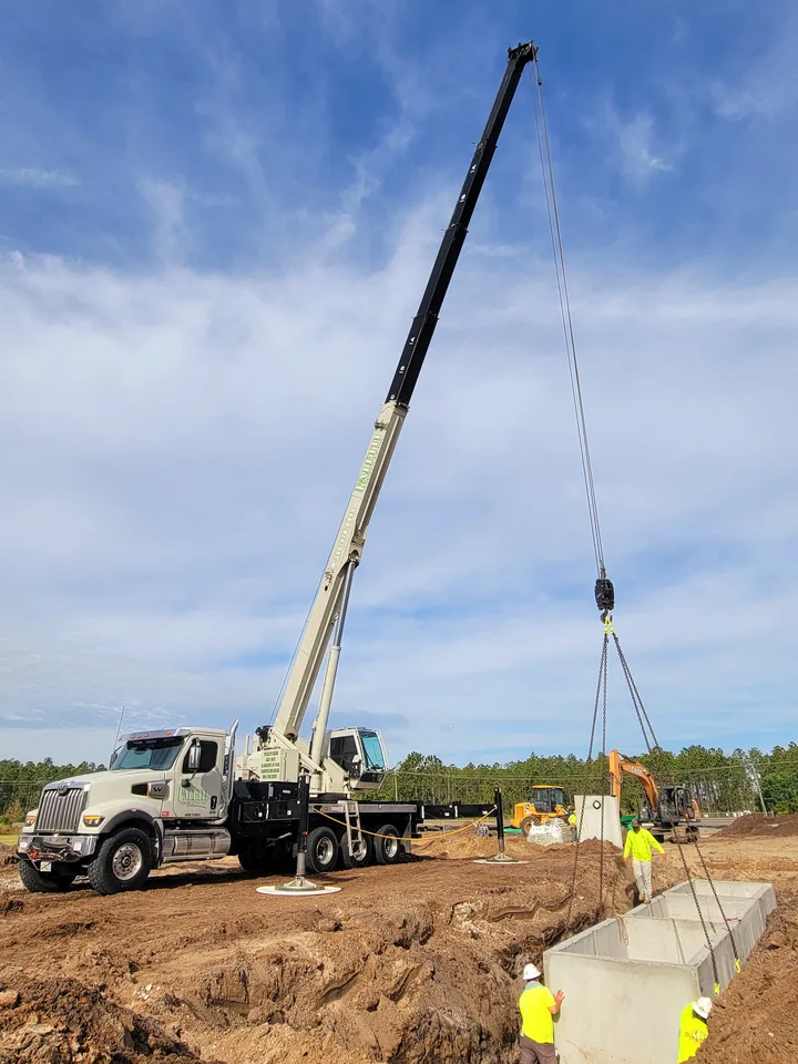 White crane and people beside a suspended concrete structure at a worksite.
