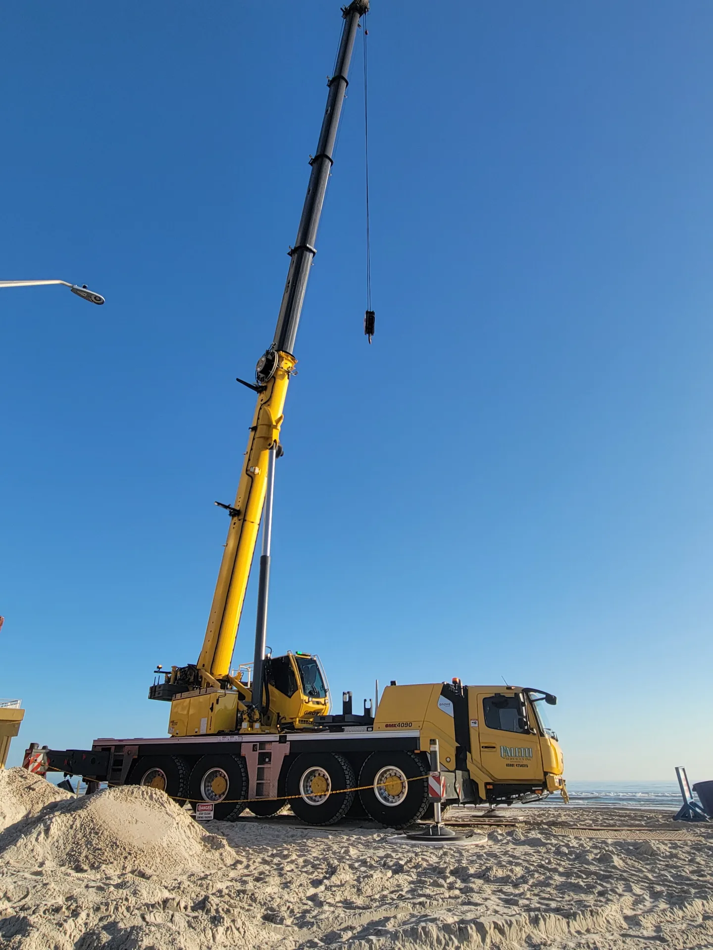 Yellow crane set up on sand beside the ocean.