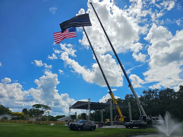 Two cranes holding flags above an outdoor stage.