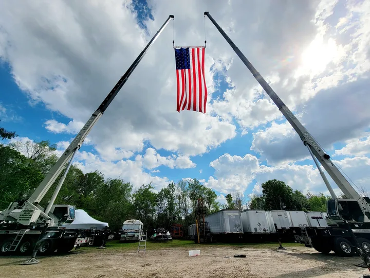 Two white crane booms supporting an American flag above a yard.