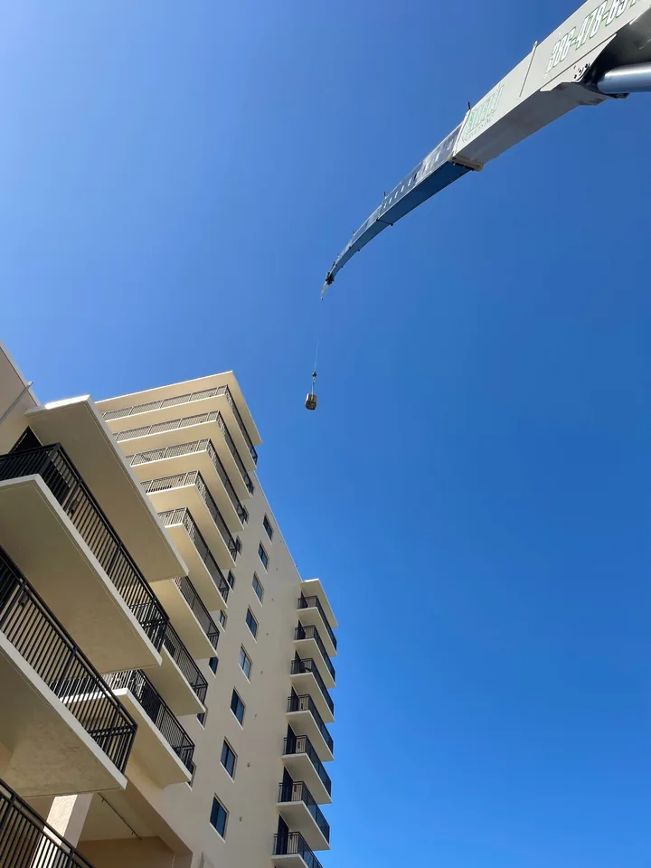 Upward view of a white crane boom beside a multi-storey building.