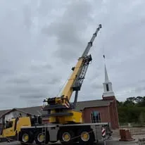 Small supplied photograph of a yellow crane beside a building with a spire.