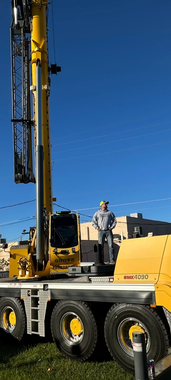 Person standing beside the raised boom of a yellow crane.
