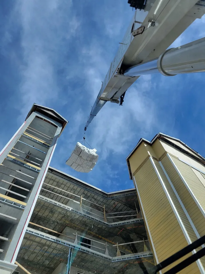 Upward view along a white boom toward a suspended load between buildings.