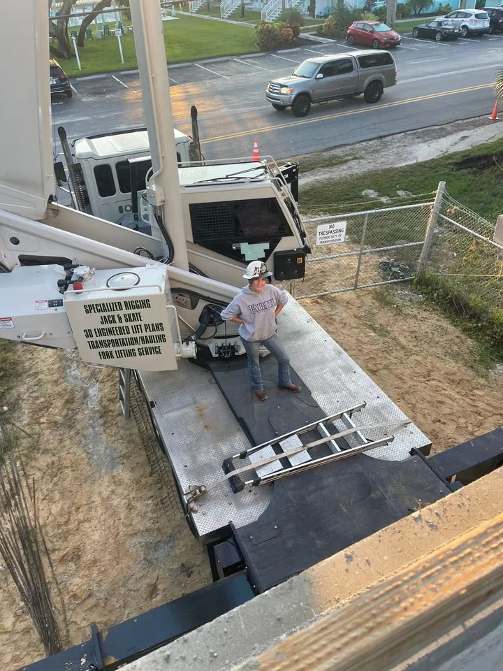 Person on the platform of a white crane truck beside a road.