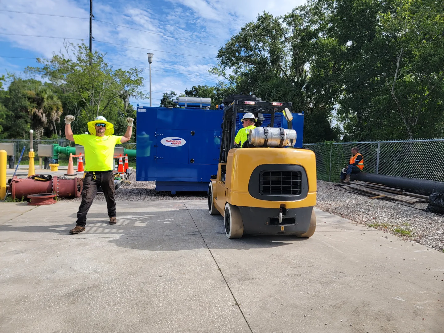 Yellow forklift and people beside a large blue equipment unit at an outdoor worksite.