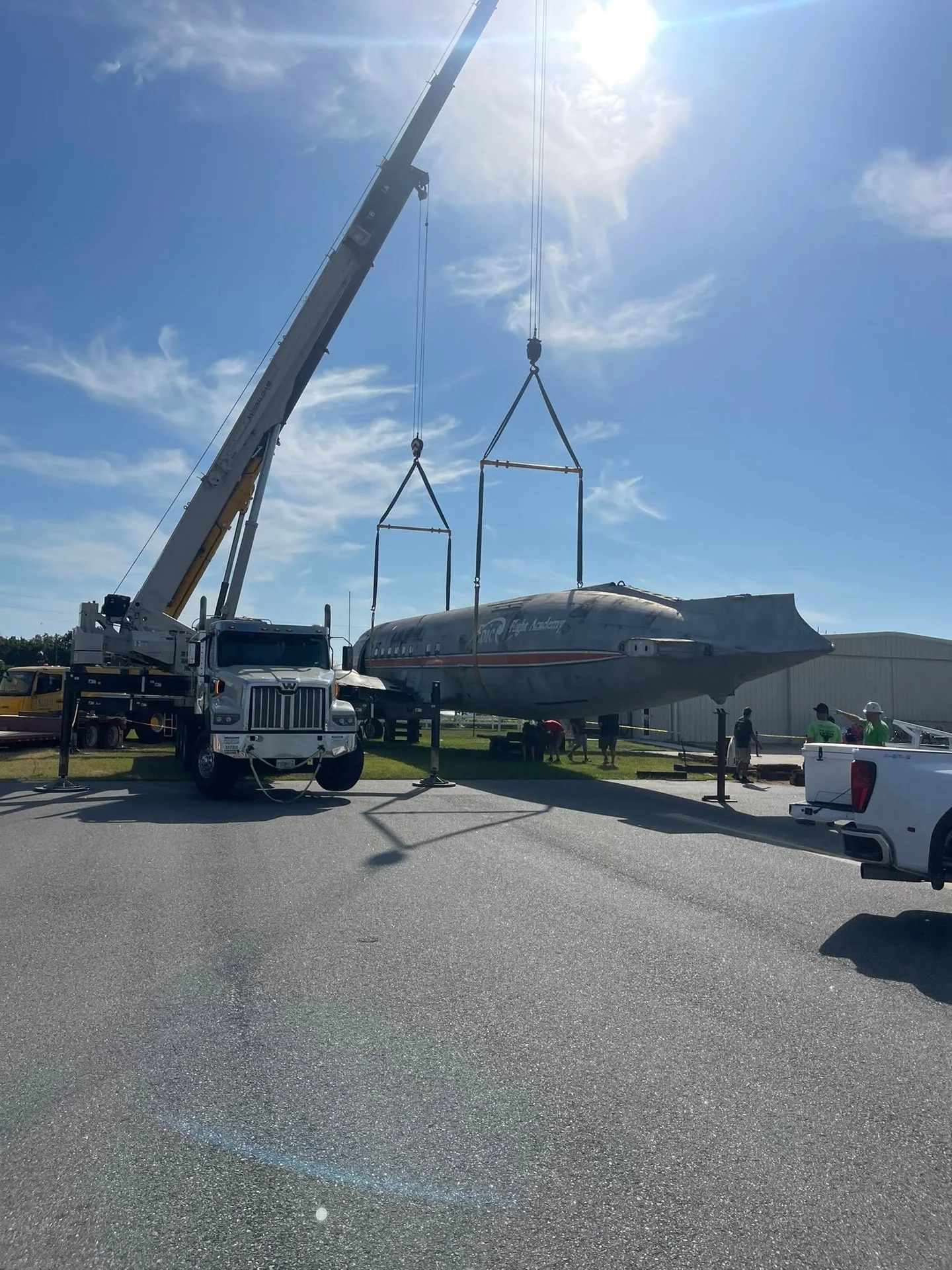 Crane rigging supporting an aircraft fuselage beside a truck-mounted crane.
