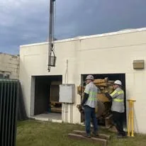 Small supplied photograph of people beside equipment at a building entrance.