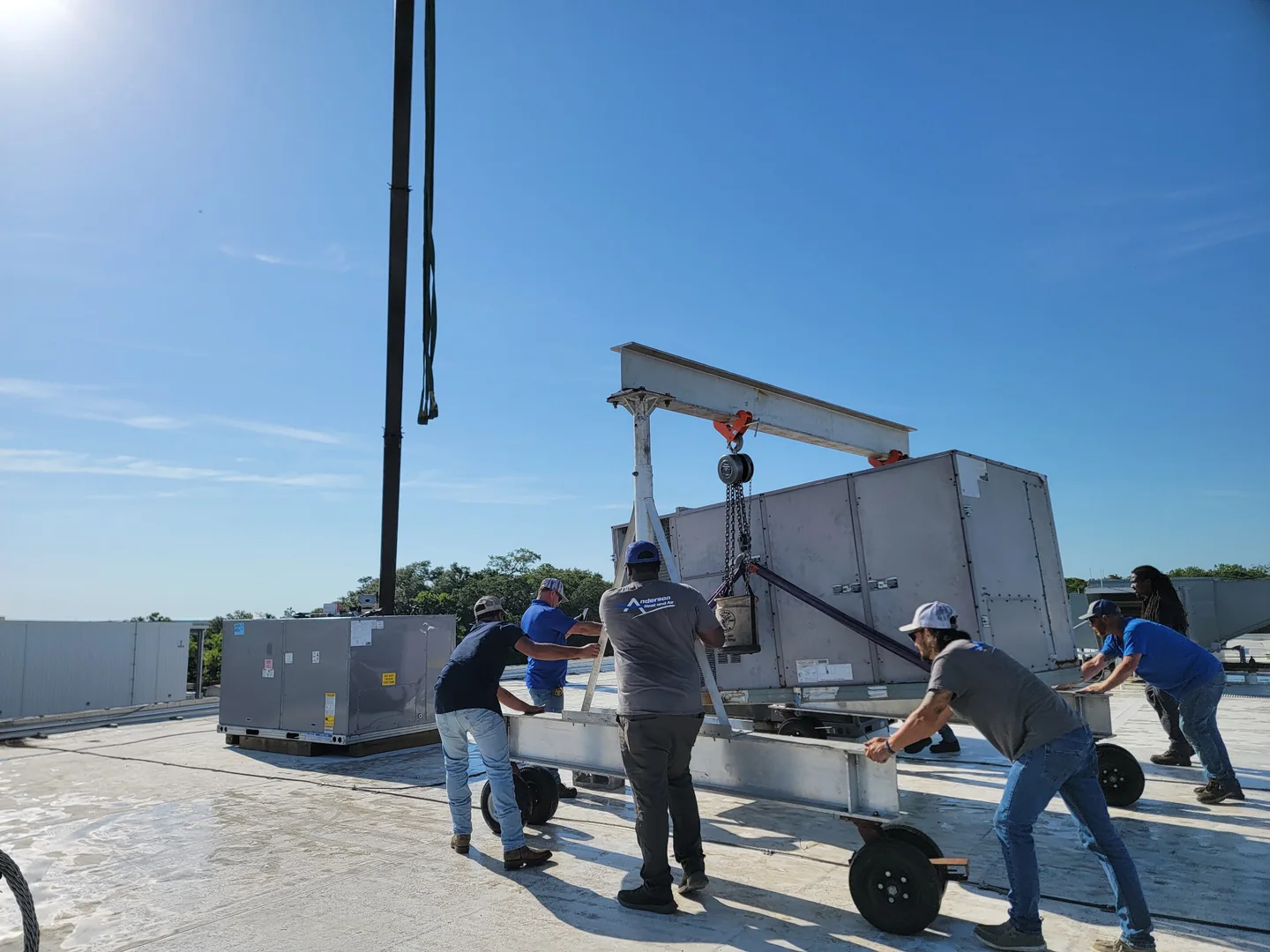 People guiding a wheeled lifting frame and large equipment unit on a rooftop.
