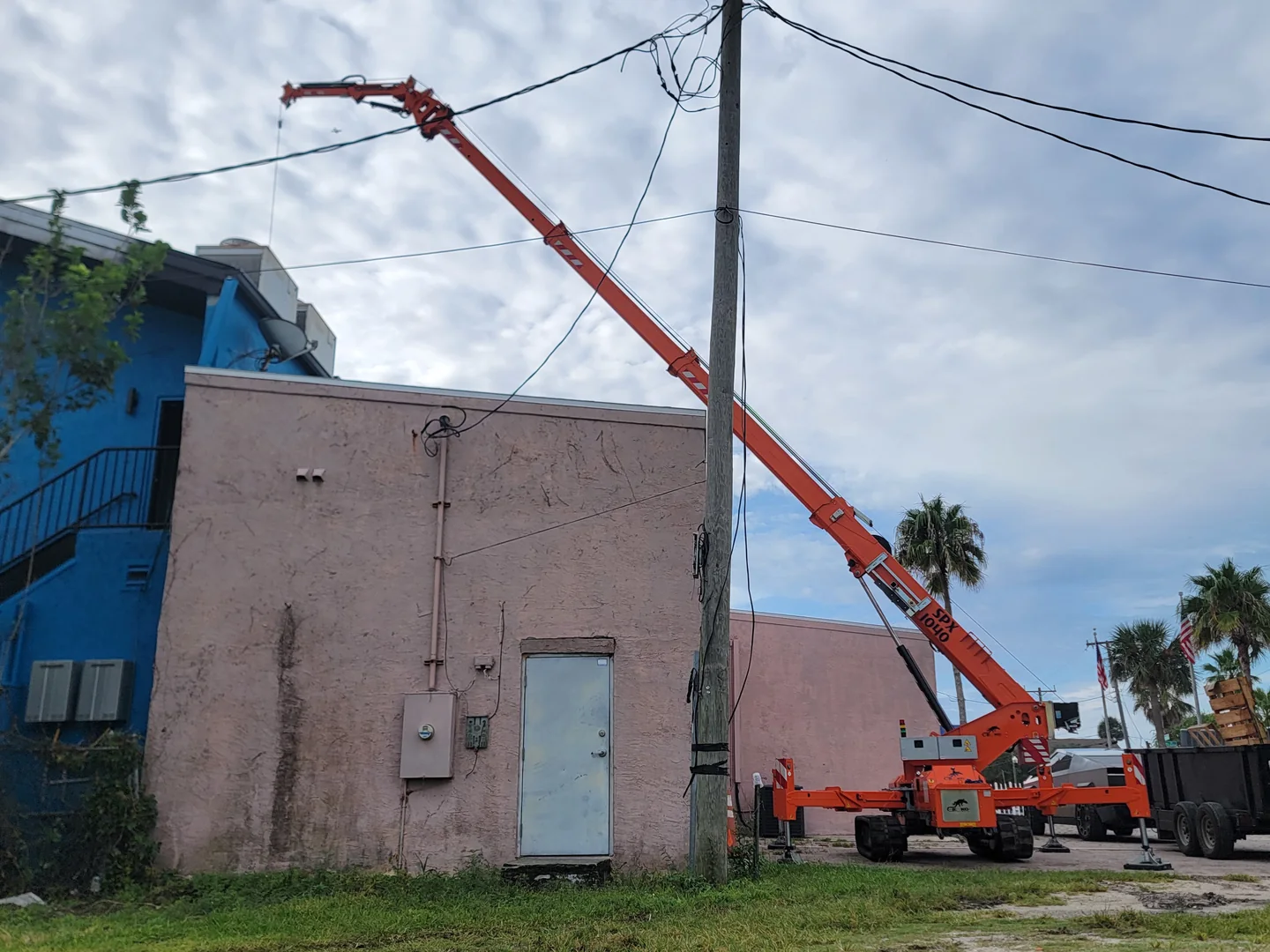 Orange compact crane with its boom extended beside a building.