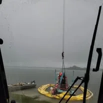 Small supplied photograph looking through a crane cab window toward a hook and equipment beside the water.
