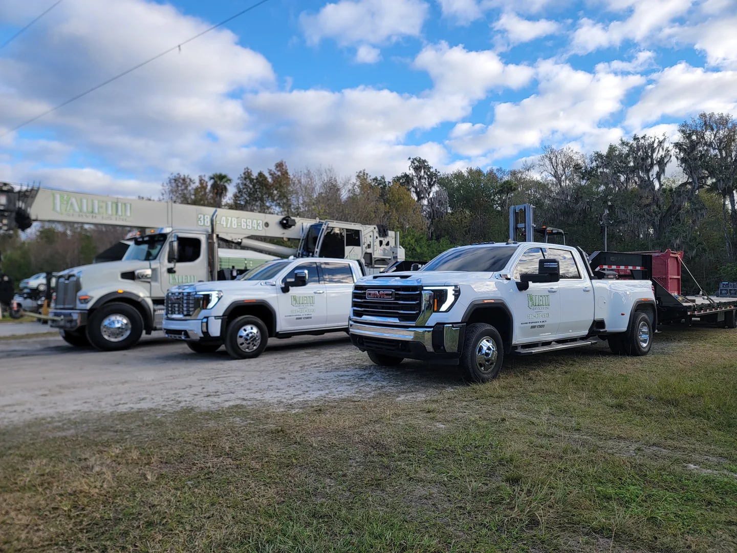 Two white Faletti pickups with a crane truck and trailer in an outdoor yard.